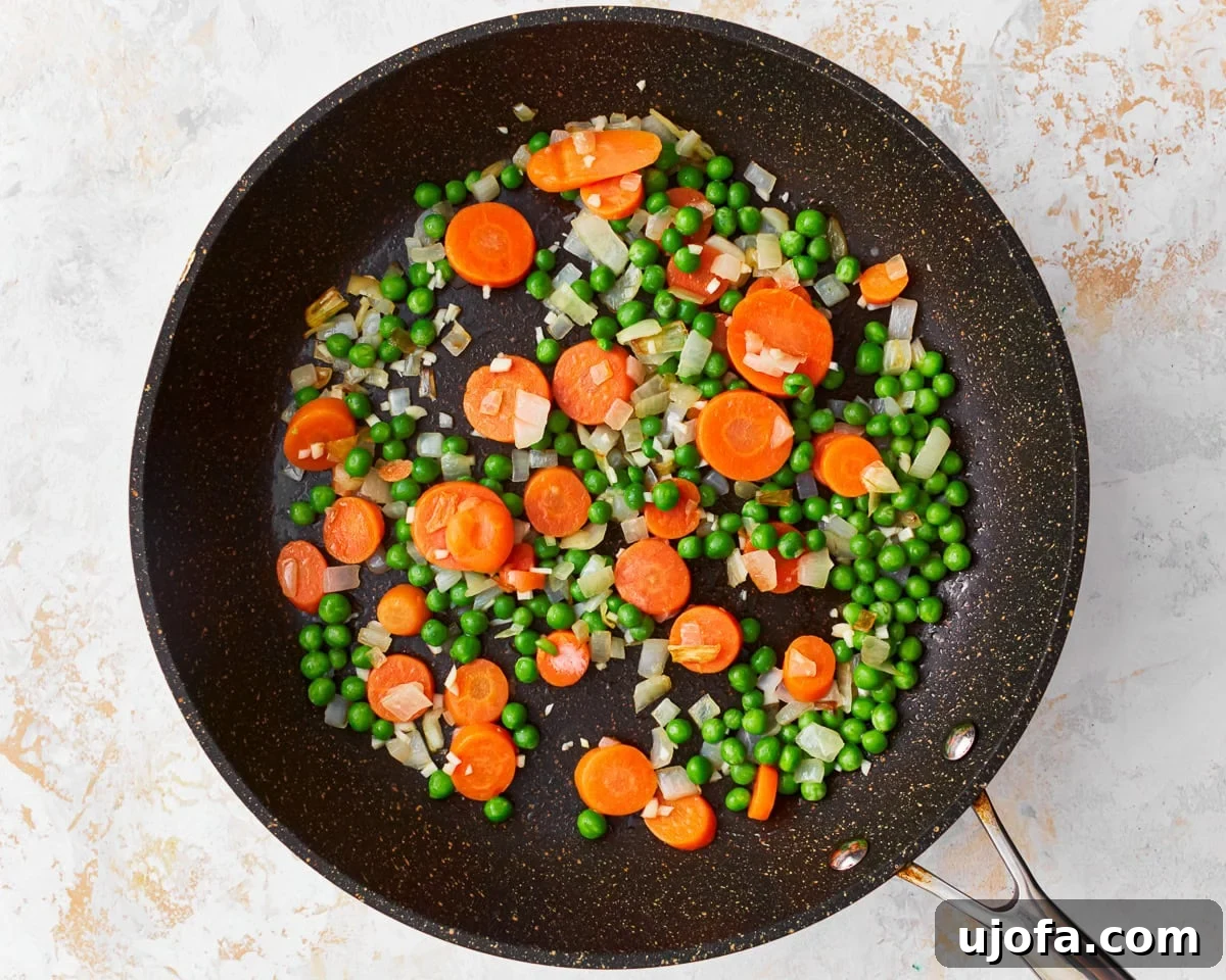 Your New Favorite Gluten-Free Fried Rice 7 Frozen peas, carrots, and diced onion cooking together in a skillet.