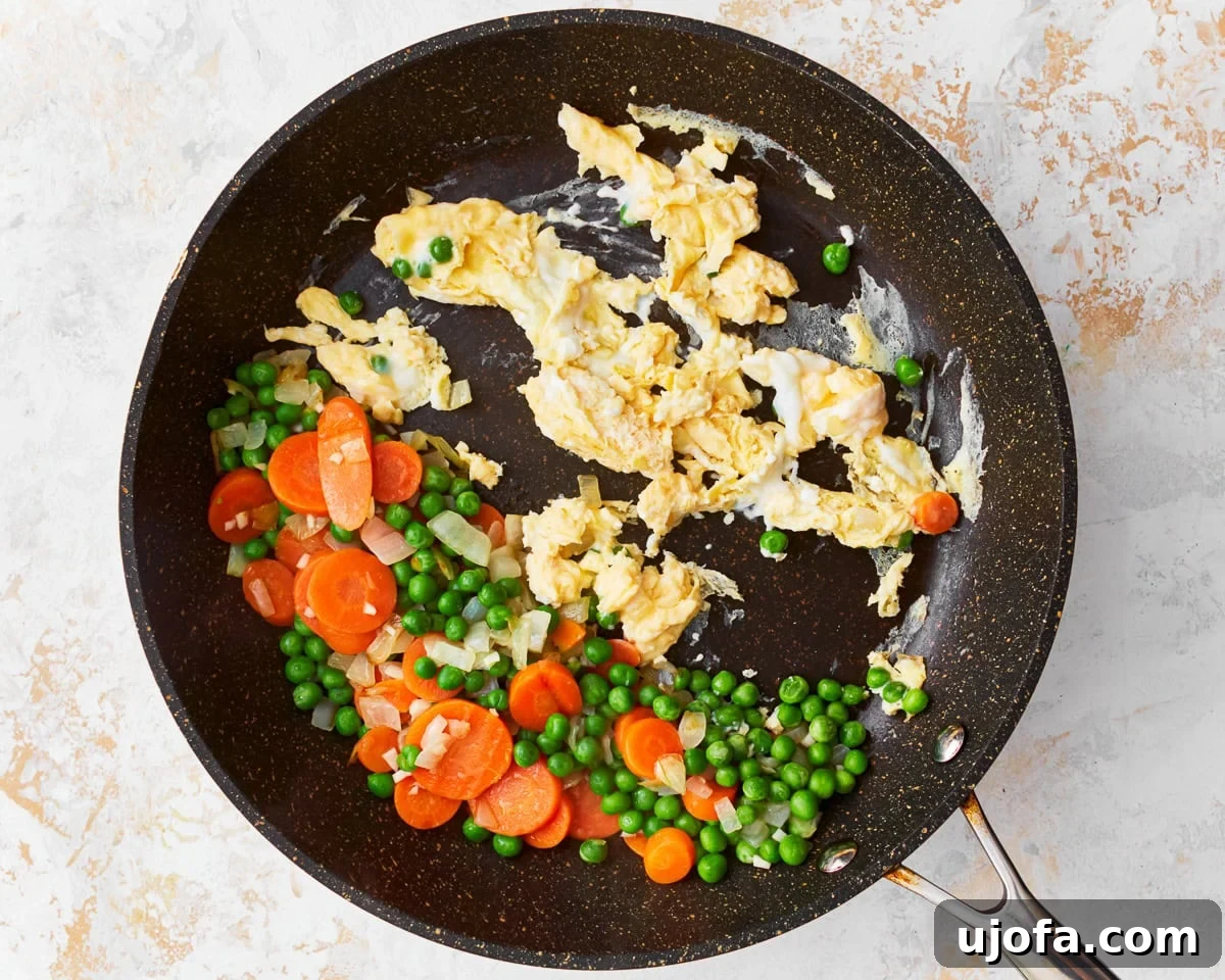 Your New Favorite Gluten-Free Fried Rice 8 Peas, carrots, and onion pushed to one side of a skillet, with scrambled eggs cooking on the other side.