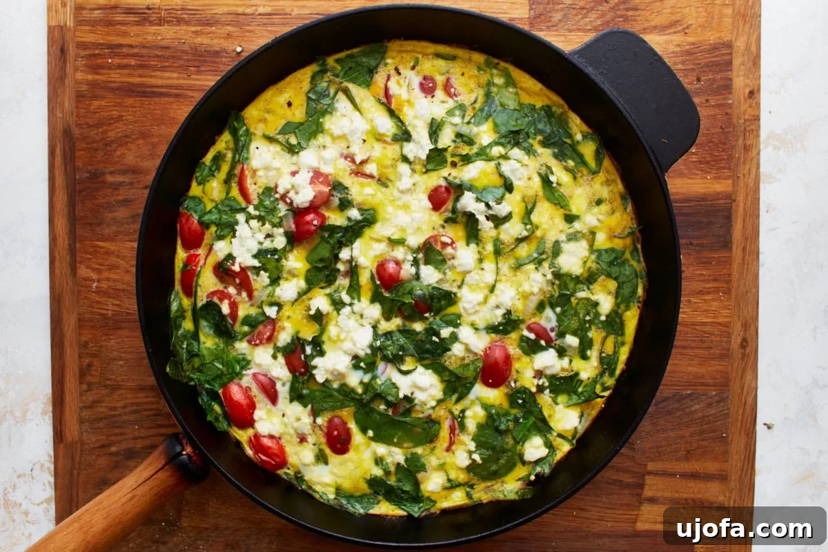 Savory Italian Egg Bake 12 A freshly baked frittata, rich with vibrant spinach, juicy tomatoes, caramelized onions, and crumbled feta cheese, rests invitingly in a black skillet.