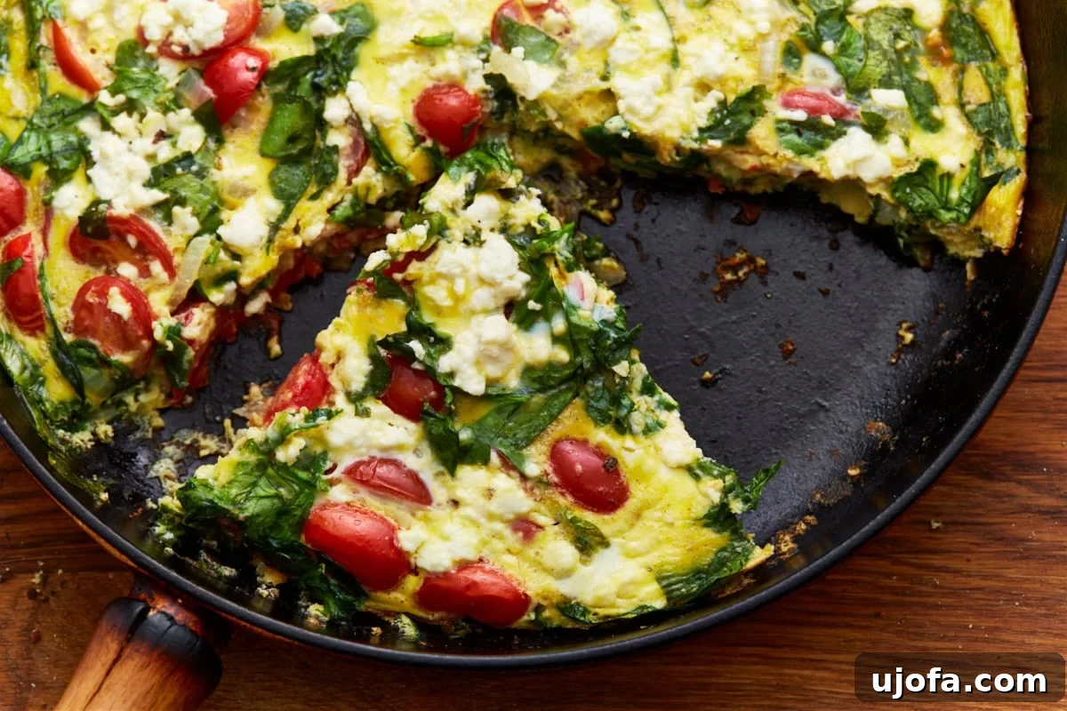 Savory Italian Egg Bake 13 A perfectly cooked slice of vegetable frittata, showcasing layers of spinach, ripe tomatoes, and crumbled feta, carefully lifted from a cast iron skillet.