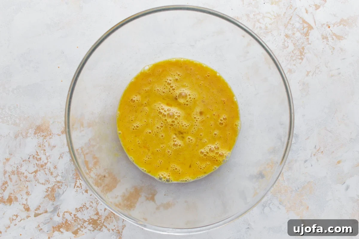 Savory Italian Egg Bake 6 A clear glass bowl containing perfectly whisked eggs, smooth and ready for the frittata, resting on a bright, minimalist surface.