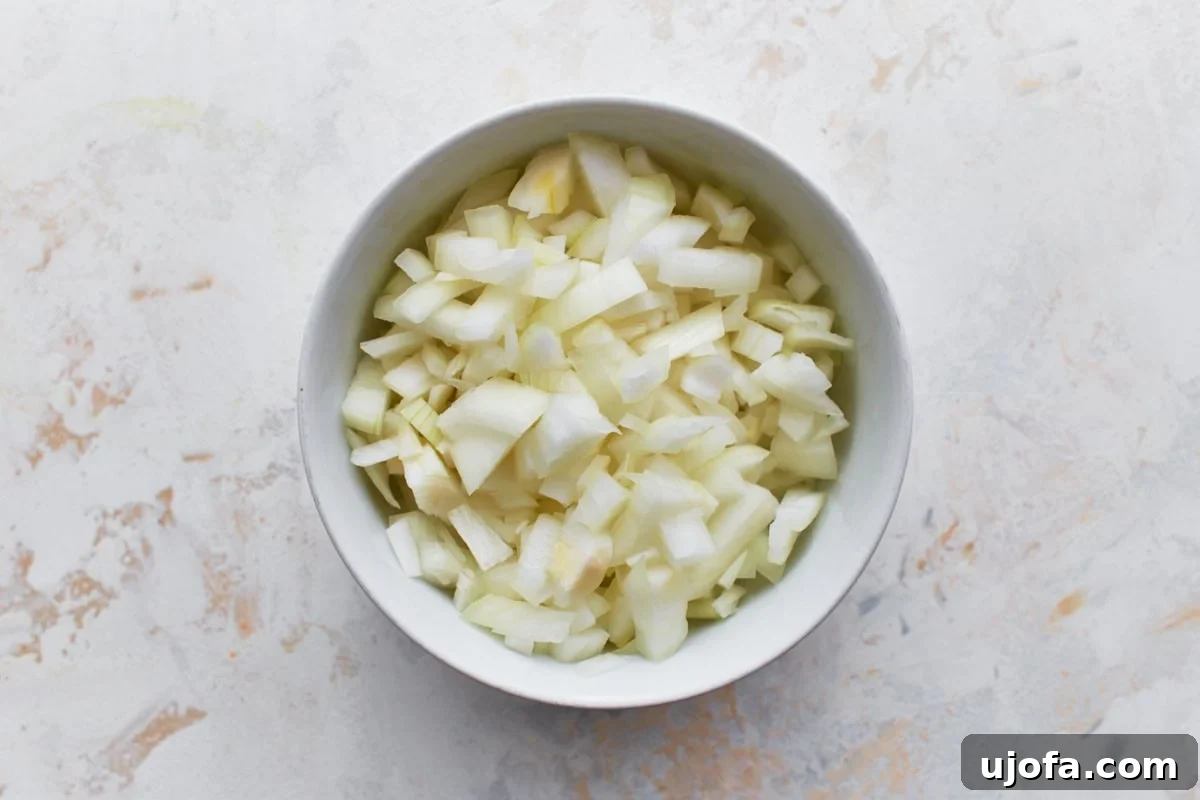 Savory Italian Egg Bake 7 Finely diced yellow onion neatly presented in a small, elegant white bowl, poised on a clean, light-colored surface.