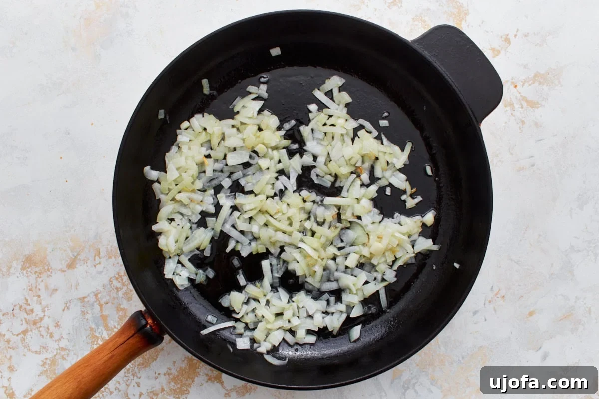 Savory Italian Egg Bake 8 Golden-brown, translucent diced yellow onions gently sautéing in a sleek black skillet with a classic wooden handle, resting on a bright, inviting surface.