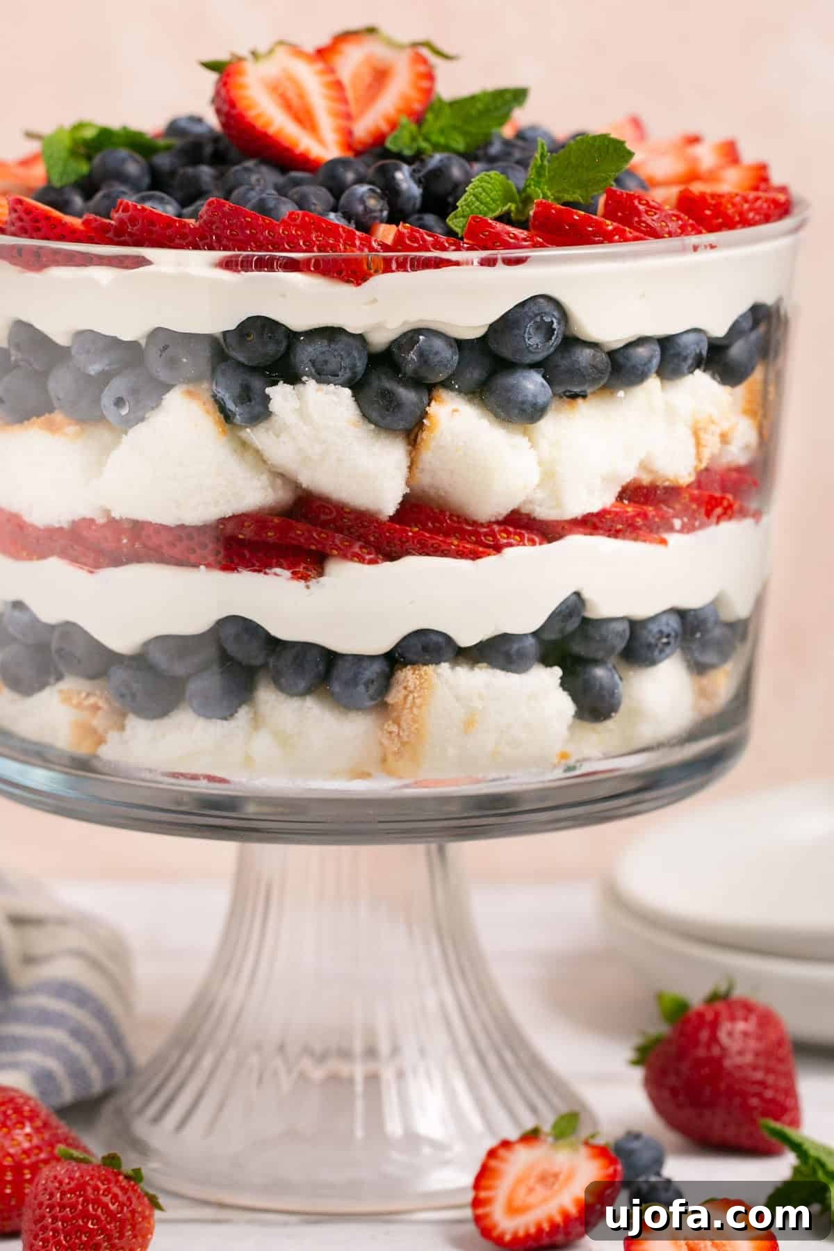 Close-up view of a beautifully layered gluten-free trifle with fresh strawberries and blueberries, garnished with a sprig of mint