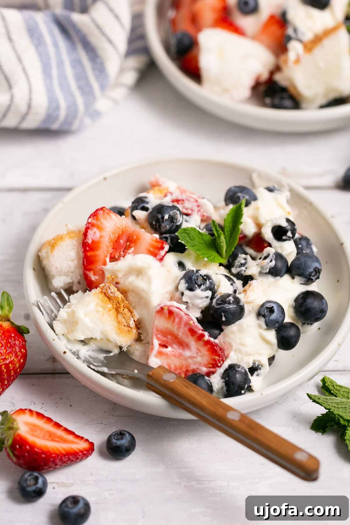 A generous scoop of gluten-free berry angel food cake trifle in a small glass bowl with a spoon, highlighting its creamy, fruity layers