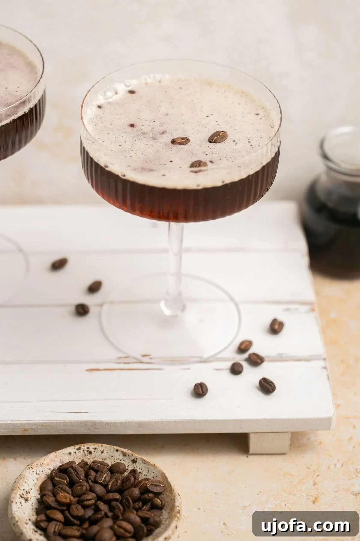 Espresso Martini Perfection Made with Kahlúa 2 A perfectly crafted espresso martini, garnished with three coffee beans, rests on a rustic wooden board surrounded by whole espresso beans.