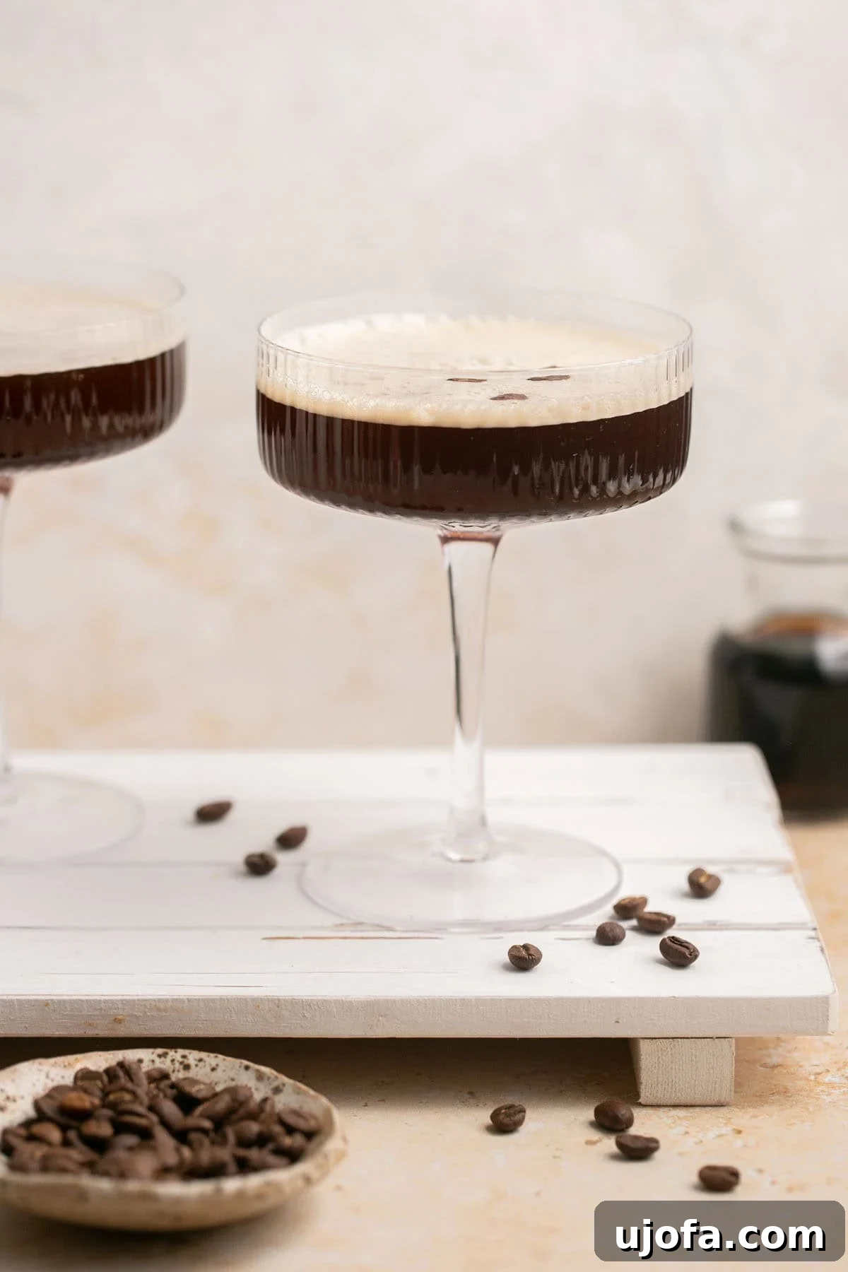 Espresso Martini Perfection Made with Kahlúa 6 Two elegantly presented espresso martinis, garnished with coffee beans, sit on a wooden serving board surrounded by more coffee beans.