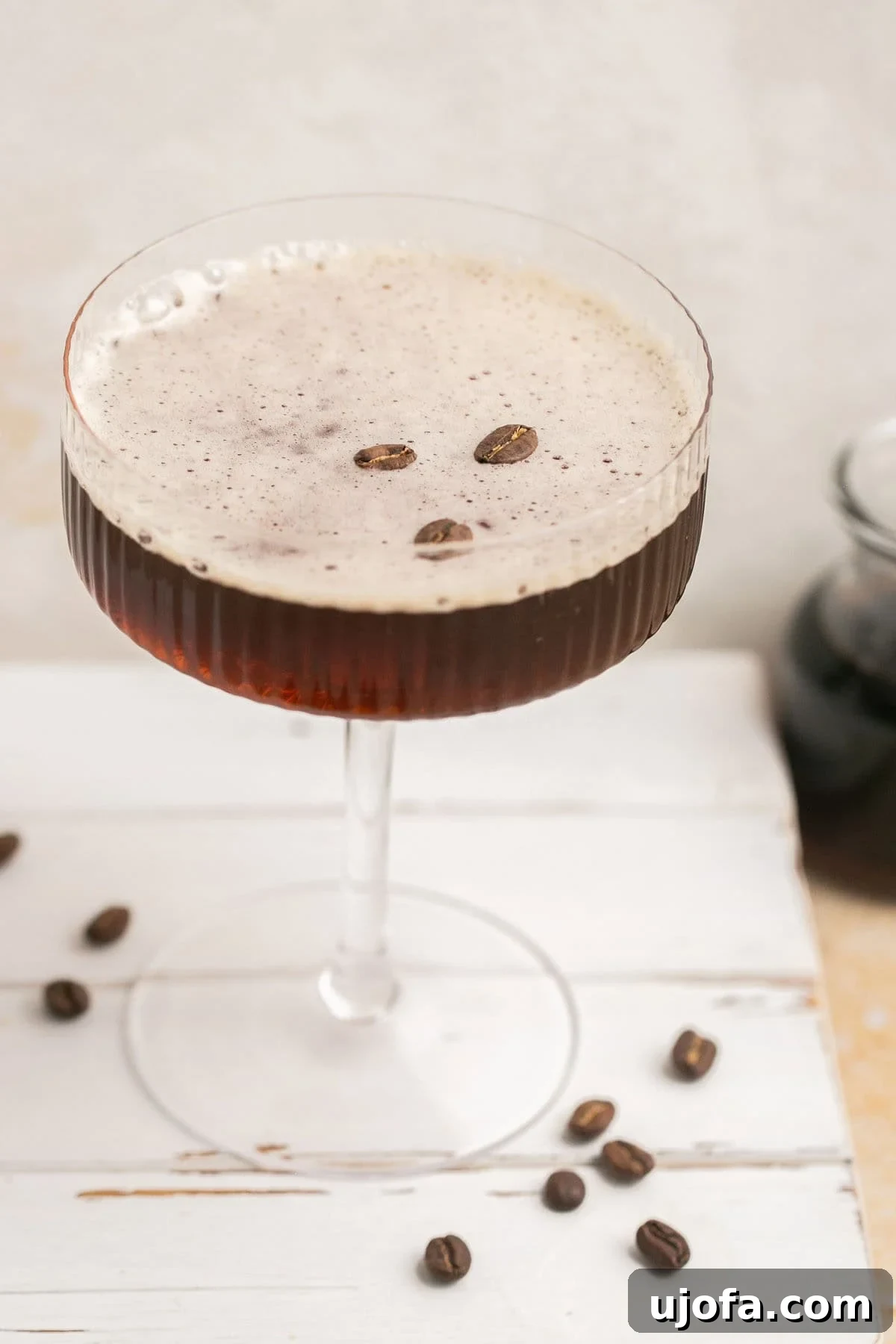 Espresso Martini Perfection Made with Kahlúa 7 A close-up shot of an espresso martini, featuring its signature frothy top and three coffee bean garnish, surrounded by scattered coffee beans.