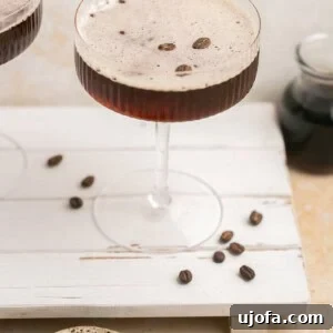 A perfectly crafted espresso martini, garnished with three coffee beans, rests on a rustic wooden board surrounded by whole espresso beans.