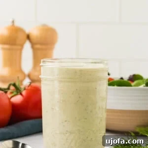 A glass mason jar filled with creamy dairy-free ranch dressing, with fresh tomatoes and dill on the side.
