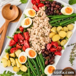 Vibrant Tuna Nicoise Salad with tuna, eggs, green beans, olives, and tomatoes on a white platter.
