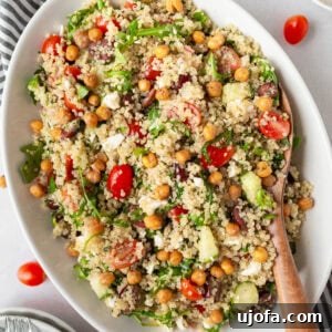 A beautiful Greek Quinoa Salad with fluffy quinoa, cherry tomatoes, cucumbers, Kalamata olives, arugula, feta, and crispy roasted chickpeas.