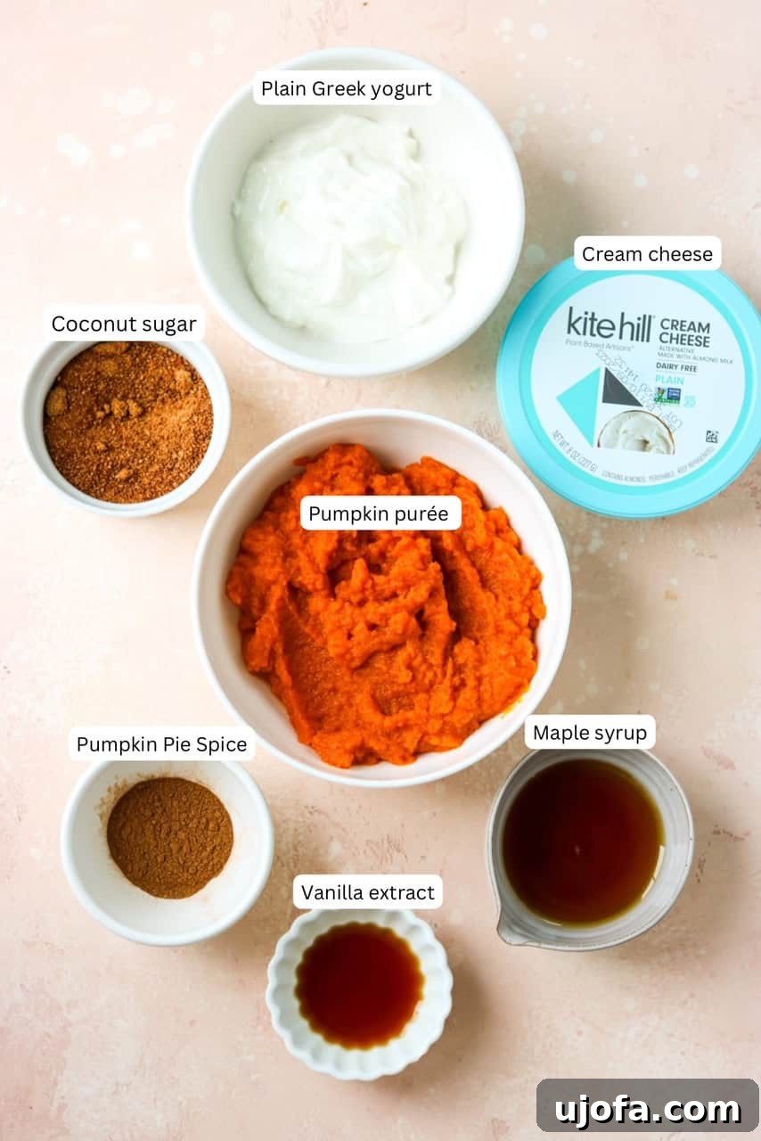 A flat lay photograph showcasing the essential ingredients for making healthy pumpkin cream cheese dip: a can of pumpkin puree, a block of cream cheese, a tub of Greek yogurt, maple syrup, pumpkin pie spice, and coconut sugar.