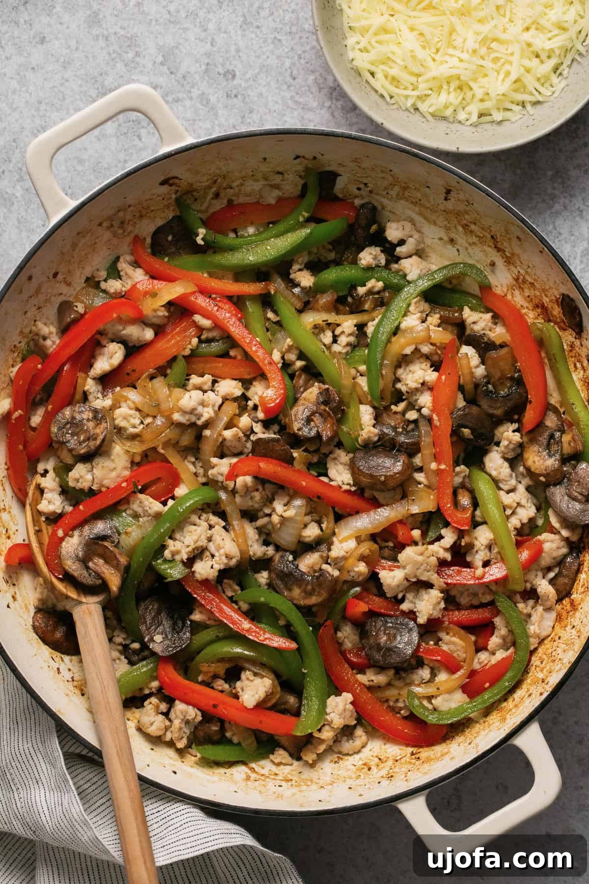 Ground chicken with peppers, onions, and mushrooms cooking in a skillet with cheese on the side