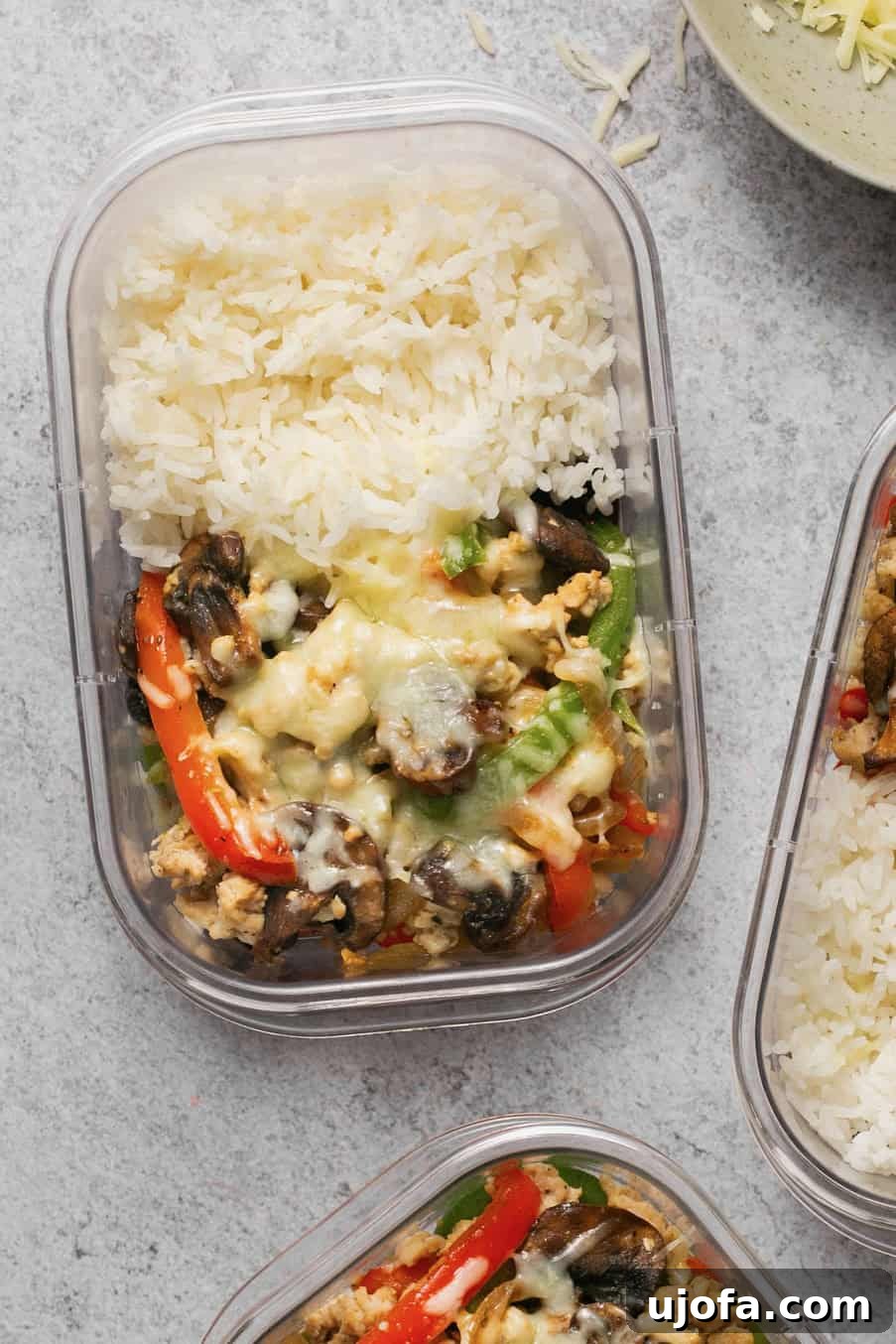 A meal prep container with chicken, veggies, rice, and melted cheese