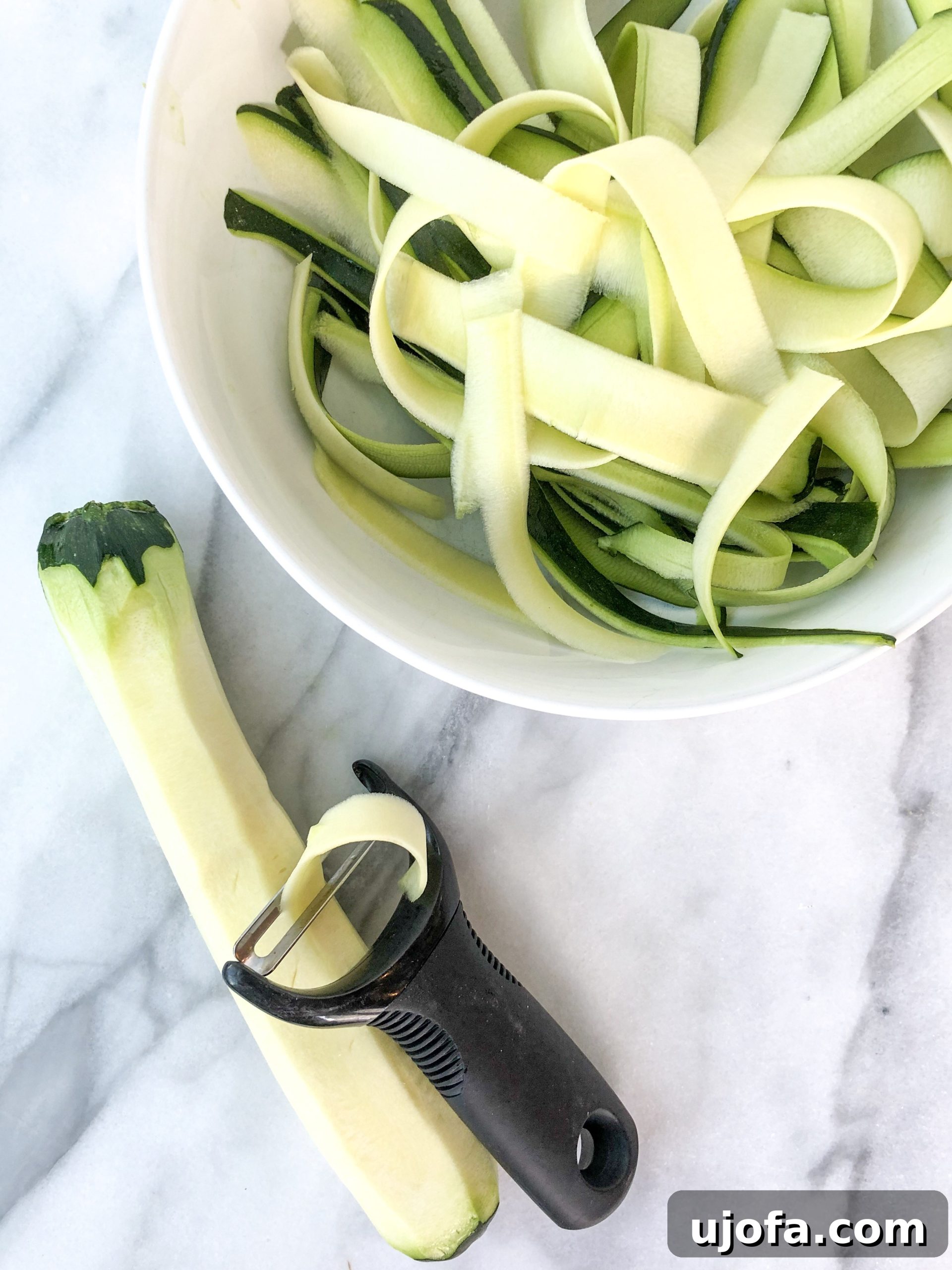 One Pan Roasted Italian Sausage and Peppers 4 Hand using a vegetable peeler to create zucchini ribbons.