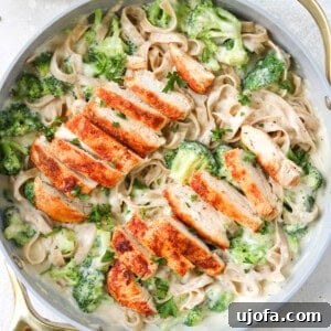 chicken and broccoli with alfredo sauce and gluten free pasta in a skillet with a napkin and a small bowl of parmesan on the side