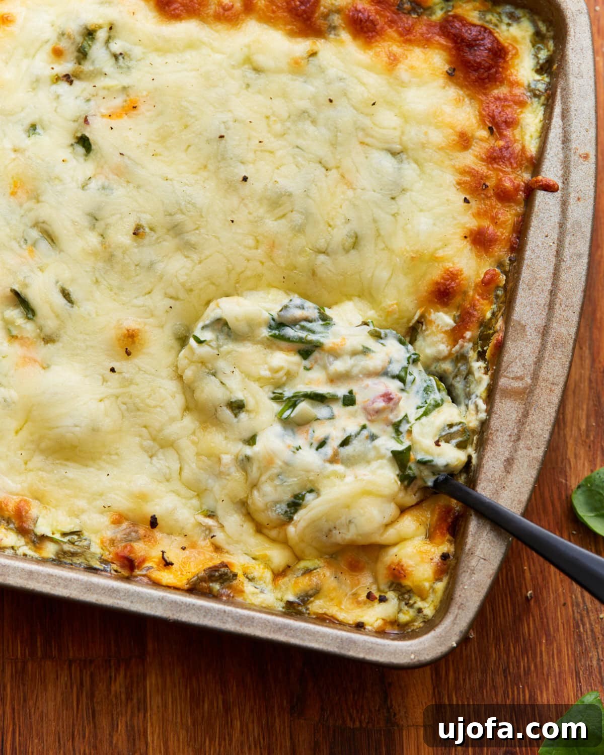 Velvety Warm Spinach Indulgence 4 spoon dipped into hot spinach dip in a tin baking dish on a wooden surface