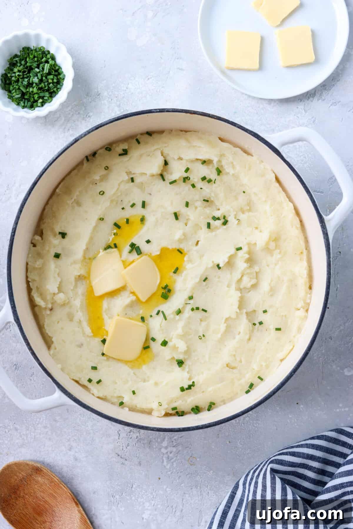 Divine Gluten-Free Mashed Potatoes 5 A close-up side view of creamy gluten-free mashed potatoes in a large pot, topped with fresh chives and a pat of melting butter