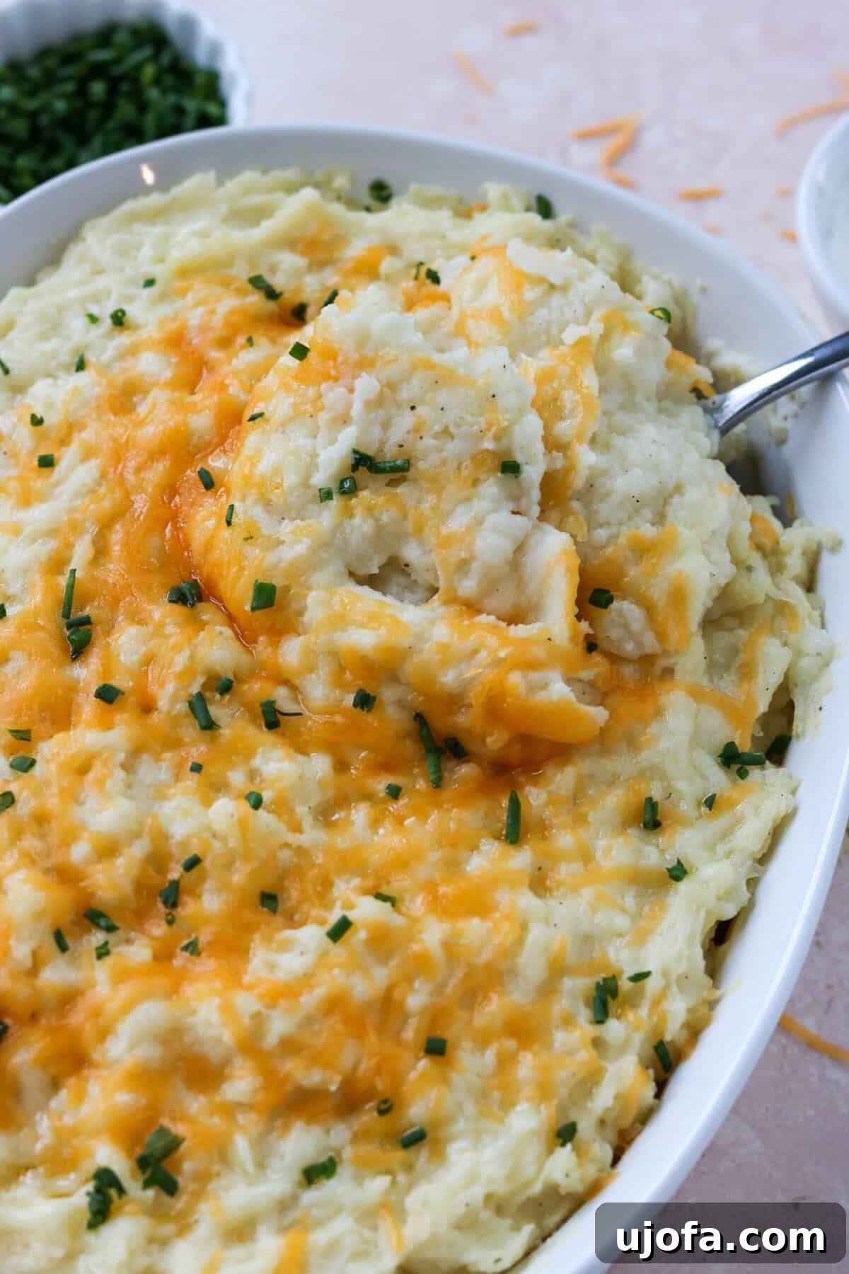 Seriously Cheesy Mash 7 A serving spoon lifting a generous scoop of cheesy mashed potatoes from a casserole dish, showing the stringy melted cheese and creamy texture.