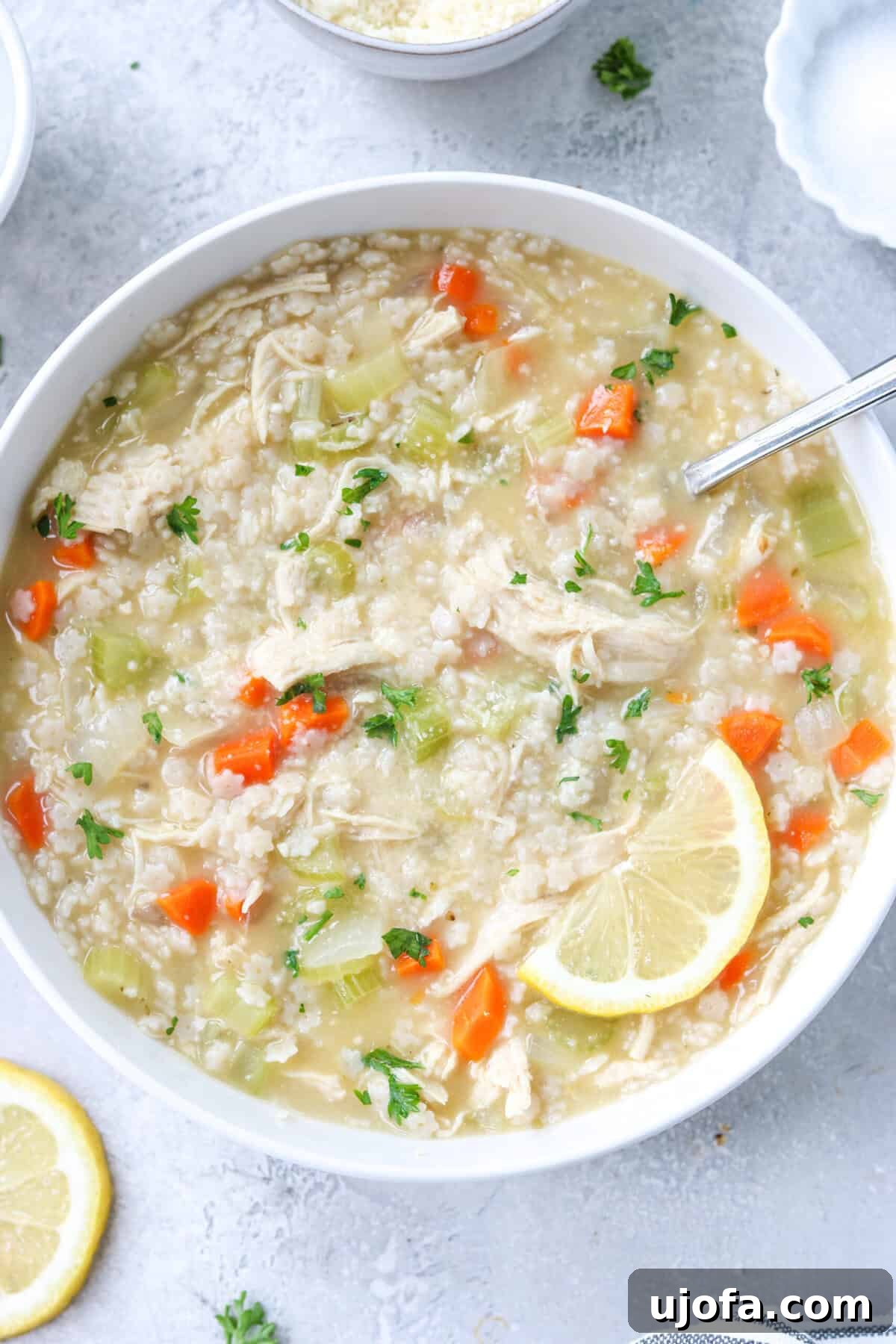 gluten free chicken pastina soup in a bowl topped with parsley and parmesan and a slice of lemon