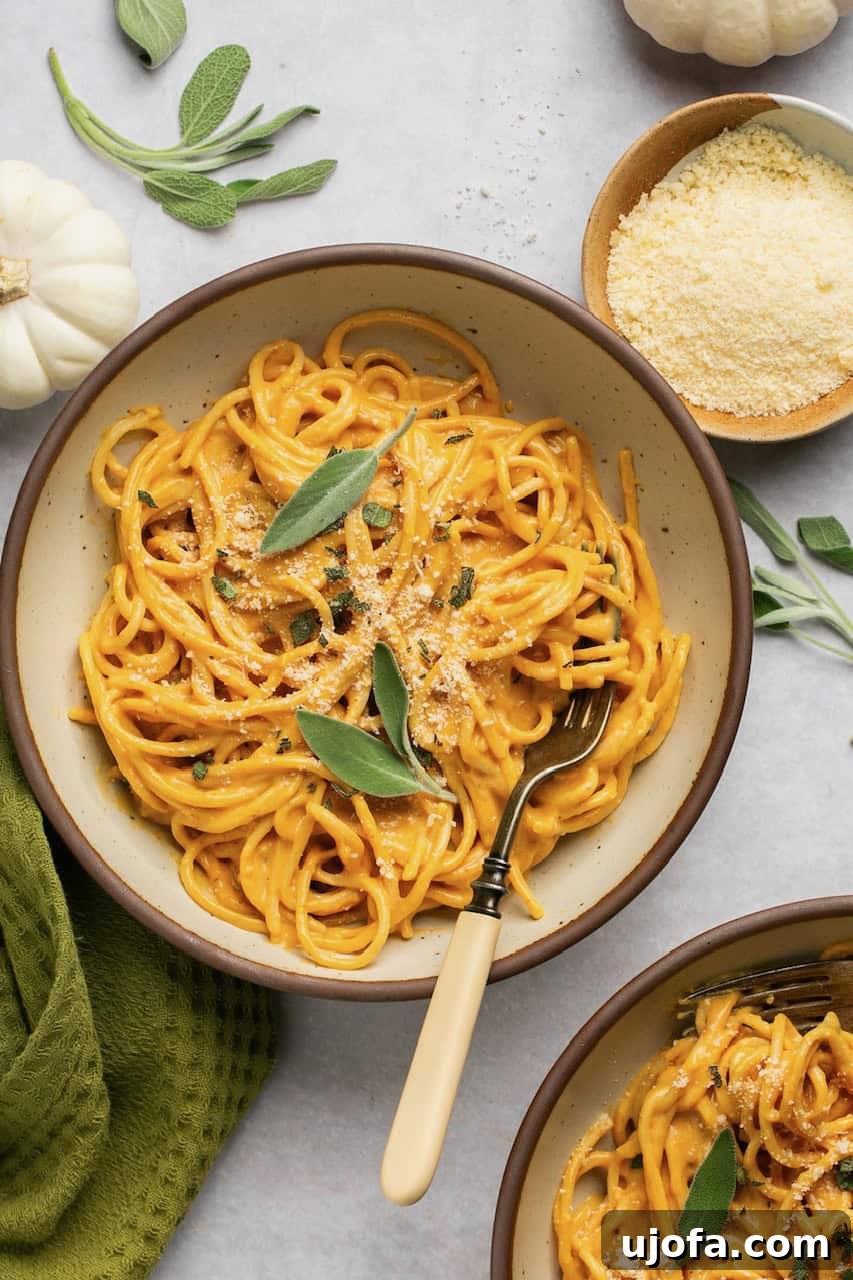 Two bowls of pumpkin pasta, garnished with fresh sage and grated parmesan cheese, with a fork resting in one bowl.