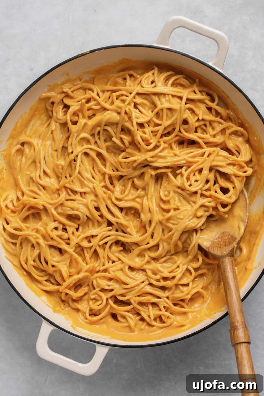 Pumpkin sauce mixed with gluten-free spaghetti in a large pot, with a wooden spoon resting inside.