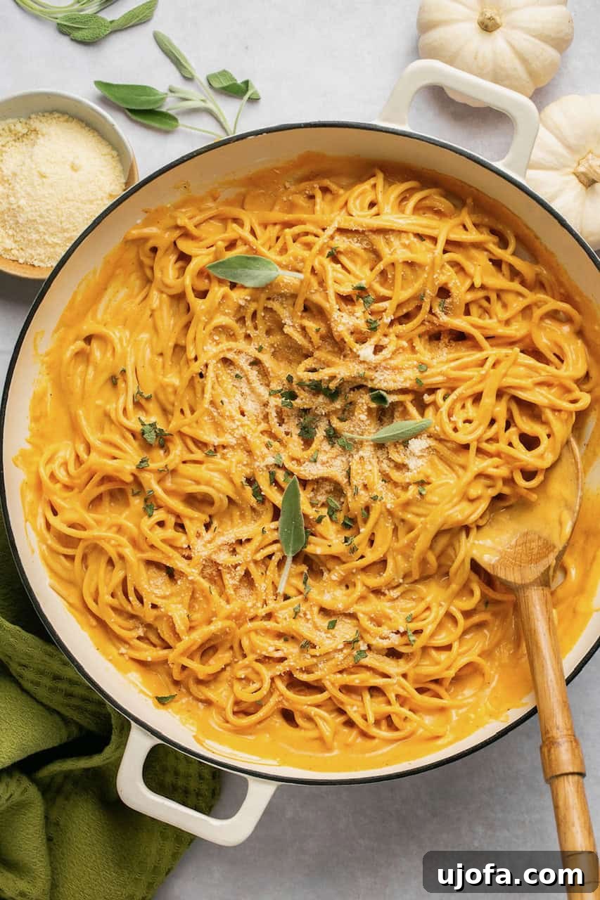 Pumpkin pasta sauce with spaghetti in a pan, garnished with fresh sage and served with a wooden spoon.