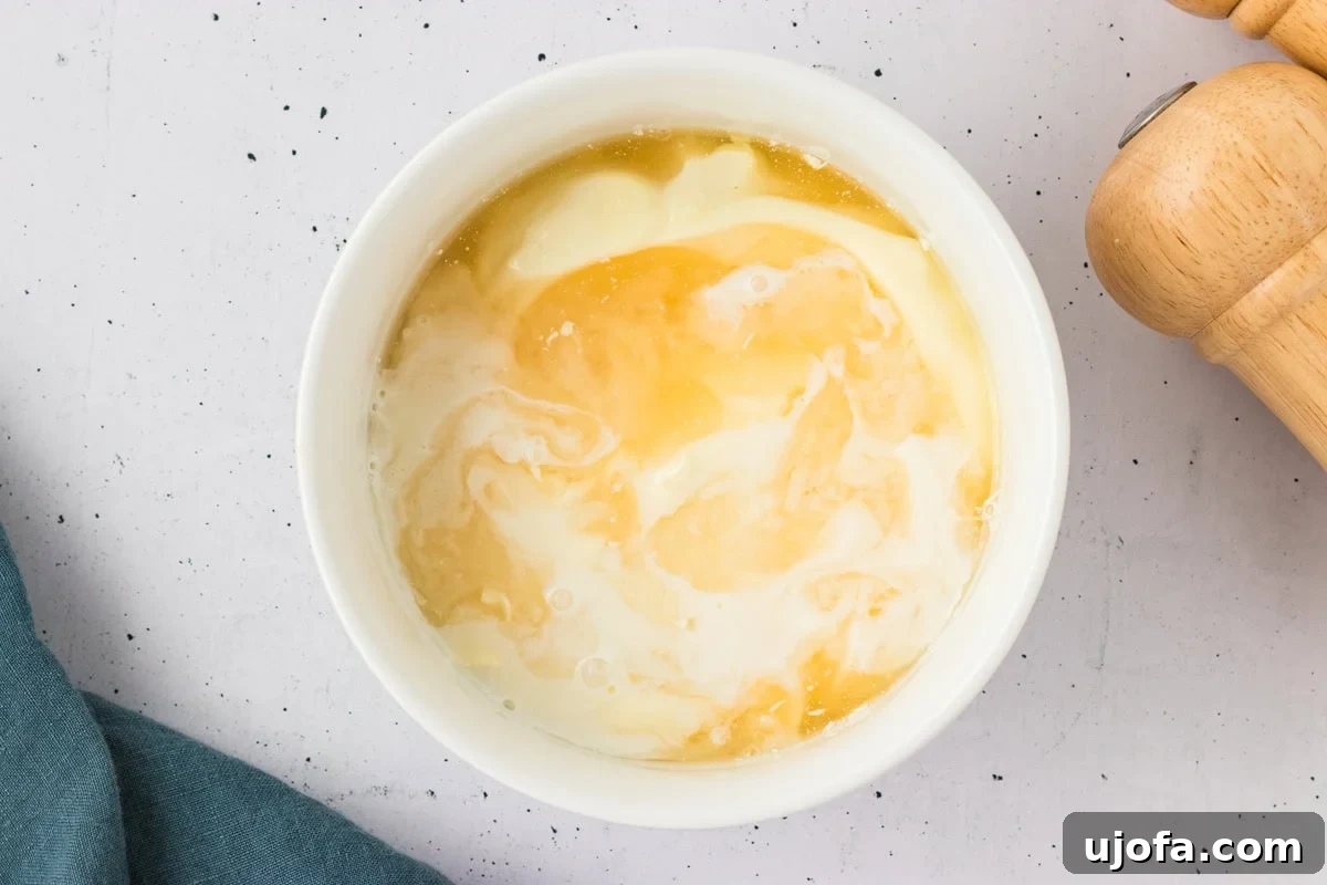Luscious Plant-Based Ranch 5 Overhead view of a white bowl with mayonnaise and vinegar beginning to mix together on a speckled white surface.