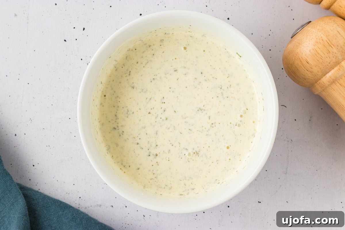 Luscious Plant-Based Ranch 7 Creamy dairy-free ranch dressing fully mixed in a white bowl, flecked with herbs and spices throughout.