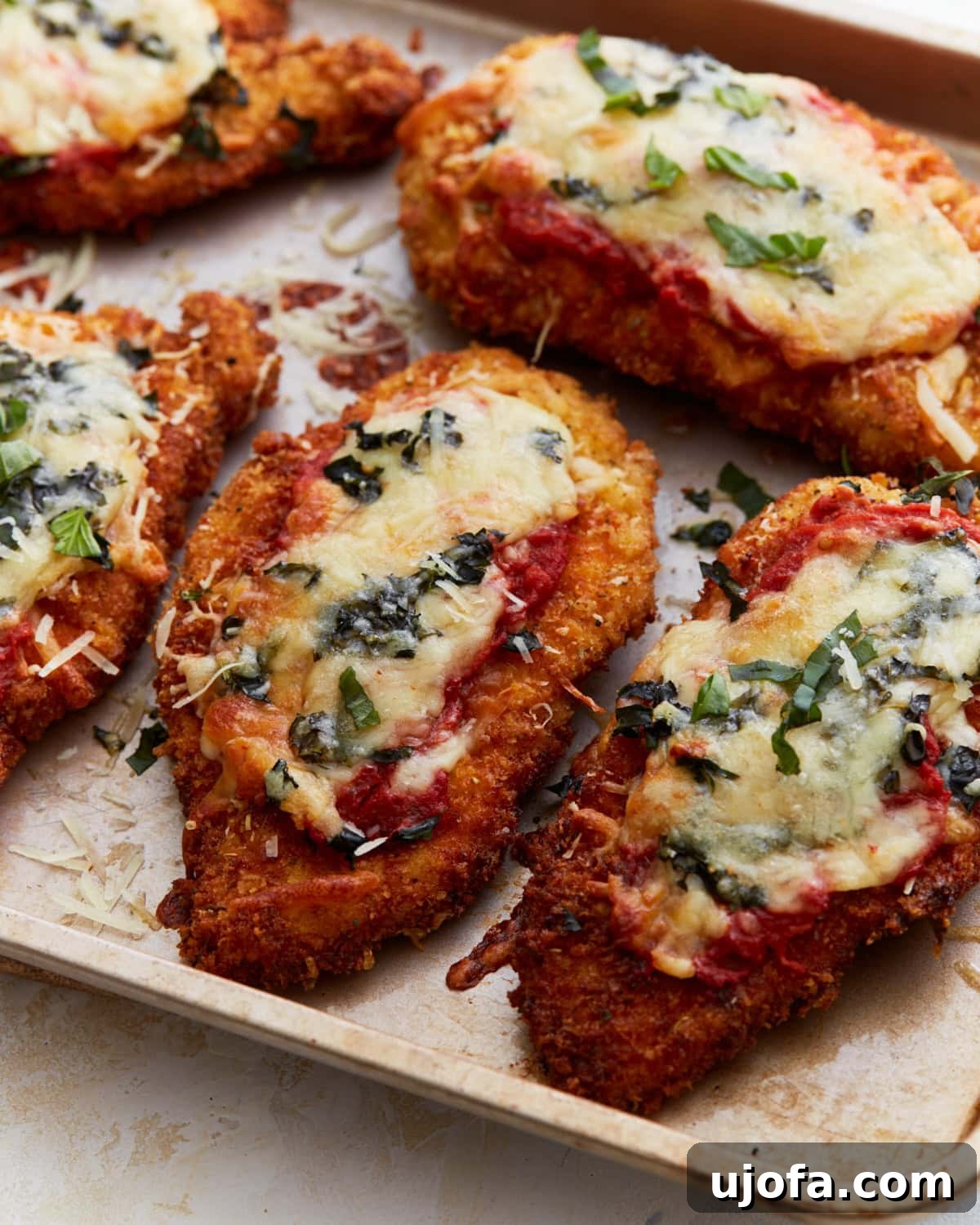 Irresistible Gluten-Free Chicken Parm 2 Crispy, golden-brown gluten-free chicken parmesan topped with melted cheese, marinara sauce, and fresh basil on a baking sheet.