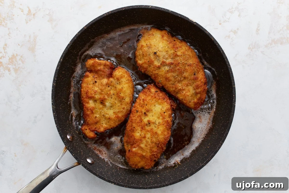 Irresistible Gluten-Free Chicken Parm 11 Three breaded chicken breasts sizzling and turning golden in hot olive oil in a large skillet on the stovetop.
