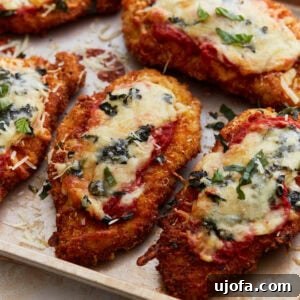 Crispy, golden-brown gluten-free chicken parmesan topped with melted cheese, marinara sauce, and fresh basil on a baking sheet.