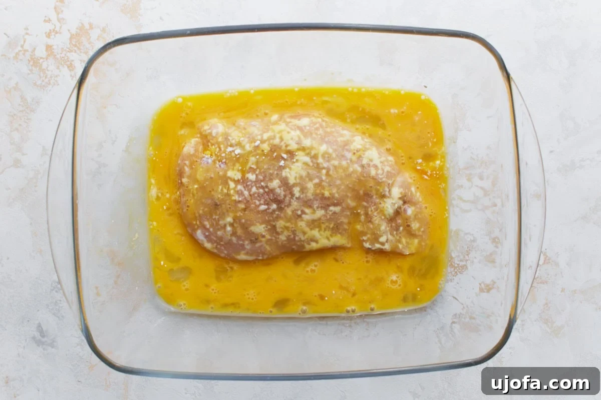 Irresistible Gluten-Free Chicken Parm 9 A flour-coated chicken breast being dipped into the whisked egg mixture, ensuring full coverage.