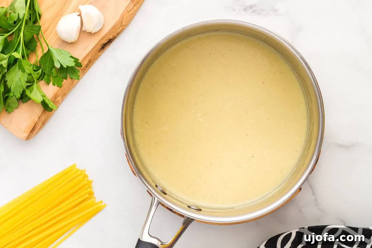 Velvety Plant-Based Alfredo 10 Dairy-free Alfredo sauce gently simmering in a pan while being continuously whisked, developing its creamy texture.