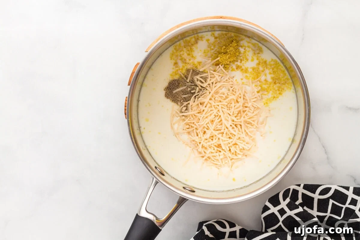 Velvety Plant-Based Alfredo 9 Dairy-free milk, Parmesan, nutritional yeast, salt, and pepper being added to the saucepan with the roux.