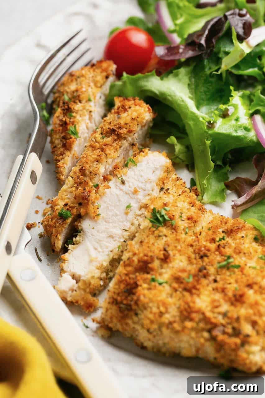 Sliced air fryer chicken cutlet on a plate with a fresh side salad and a lemon wedge, showcasing its crispy exterior and juicy interior.