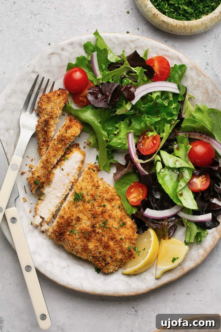 Close-up of crispy chicken cutlets, perfectly sliced to reveal their juicy interior, served next to a fresh green salad.