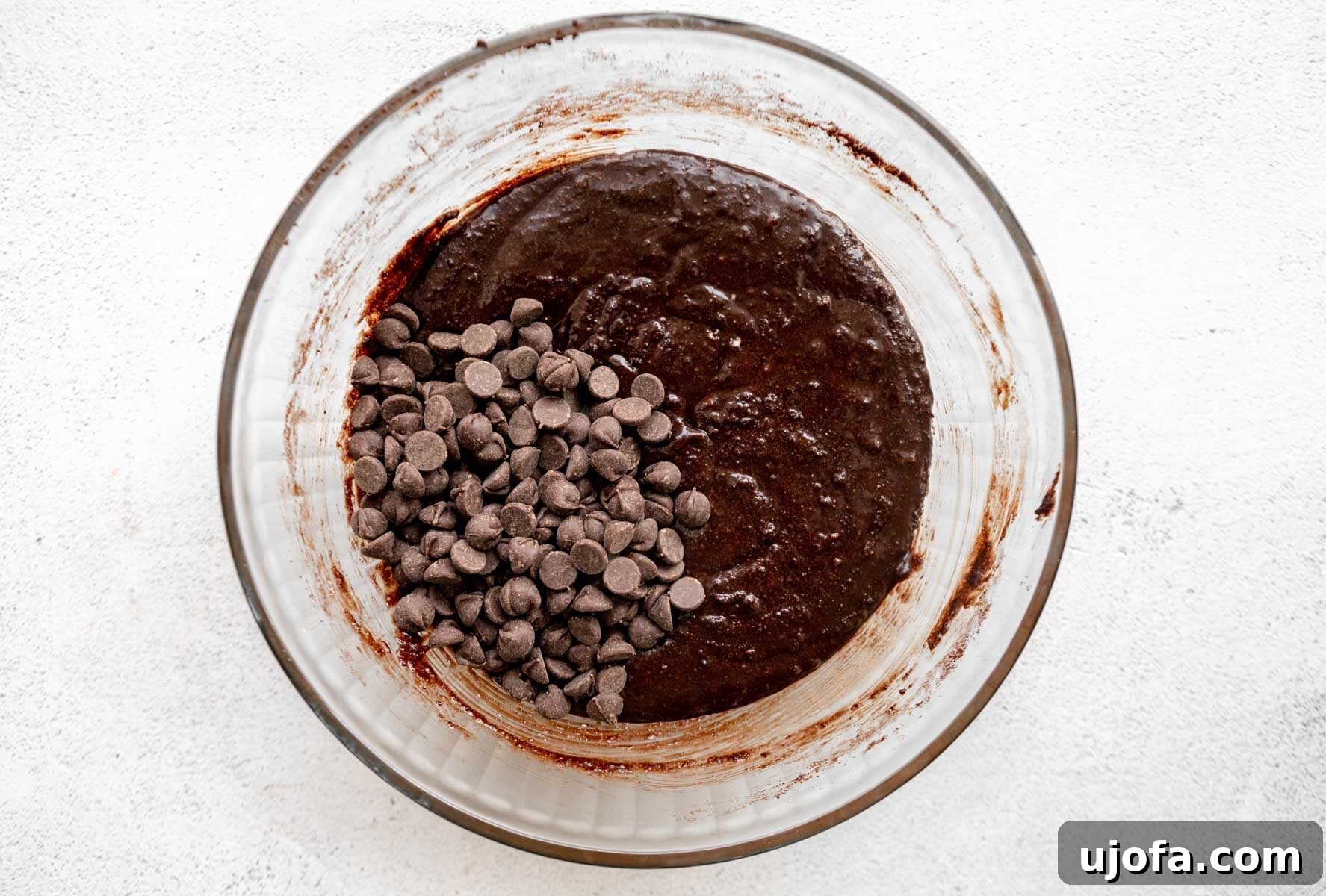Almond flour brownie batter mixed with chocolate chips, showcasing its rich texture in a glass mixing bowl.