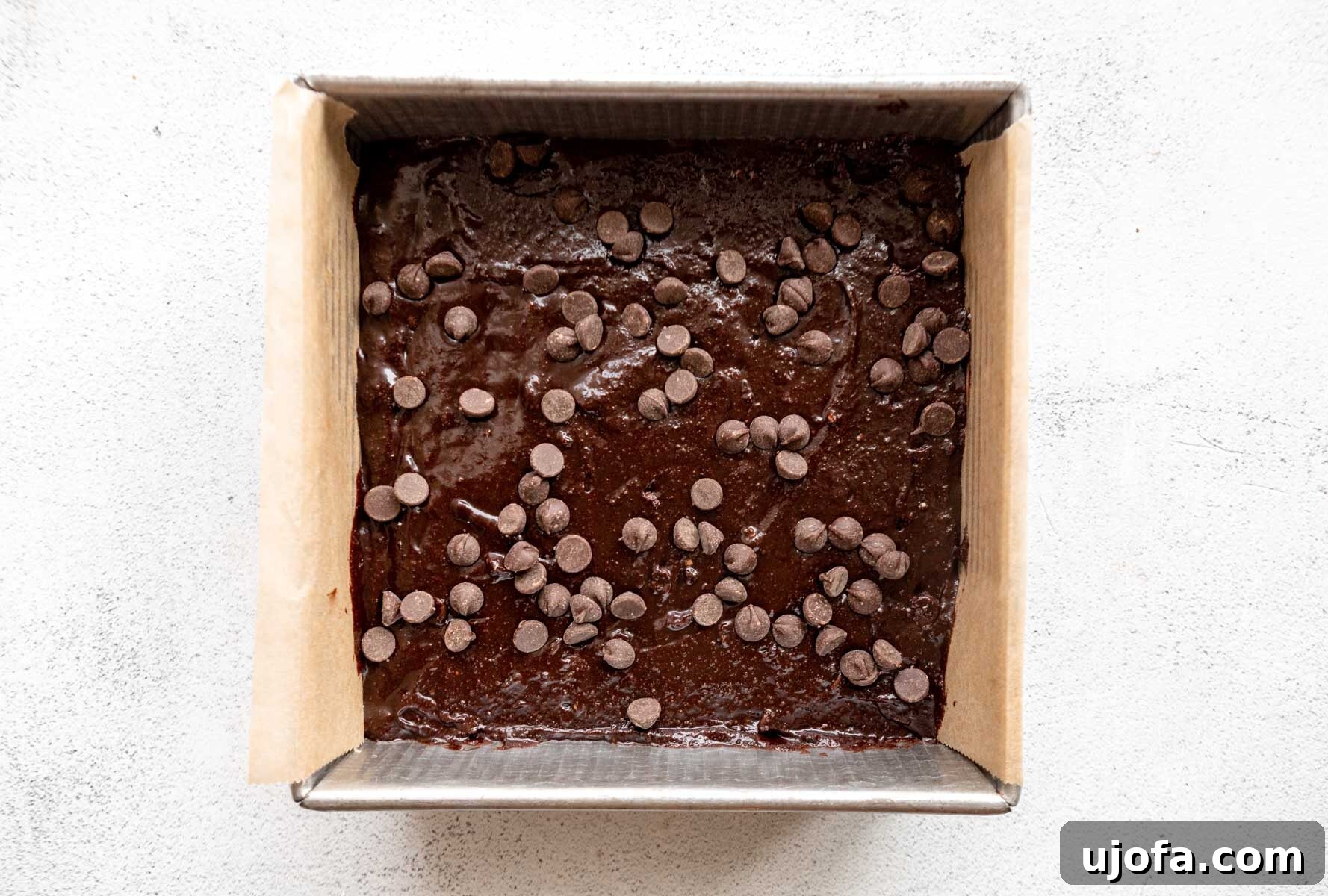Almond flour brownie batter perfectly spread in a baking pan and topped with extra chocolate chips before baking.