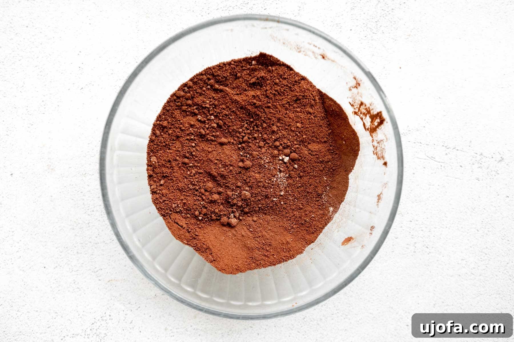 Dry ingredients for almond flour brownies in a glass mixing bowl, including almond flour and cocoa powder.
