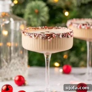 peppermint espresso martini with a candy cane rim with a Christmas tree in the background surrounded by ornaments
