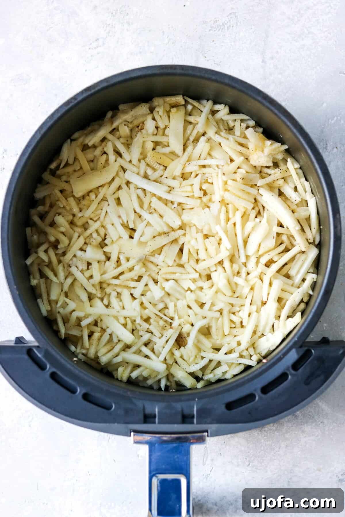 frozen hash browns spread in a single layer in an air fryer basket