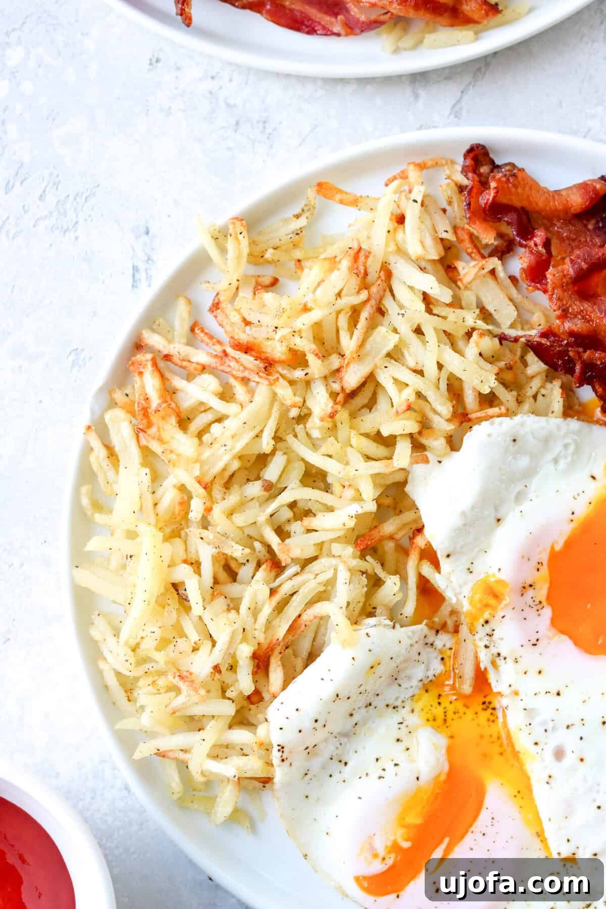 a close up of cooked hash browns on a plate with eggs and bacon, showing their crispy texture