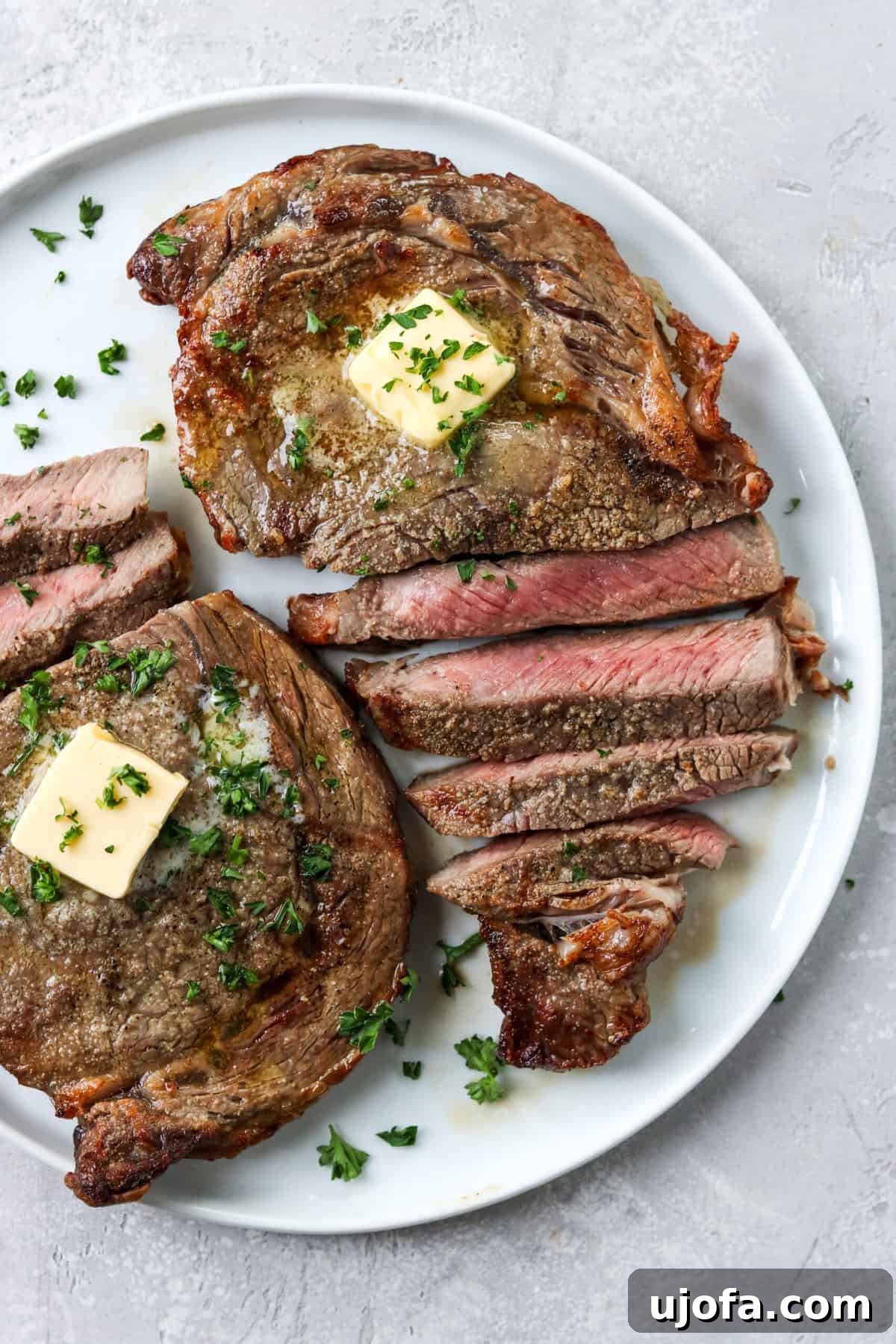Expertly sliced steak presented on a pristine white plate, garnished with melting butter and fresh parsley.