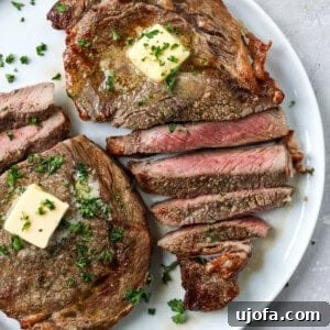 Sliced air fryer ribeye steak on a white plate topped with butter and parsley
