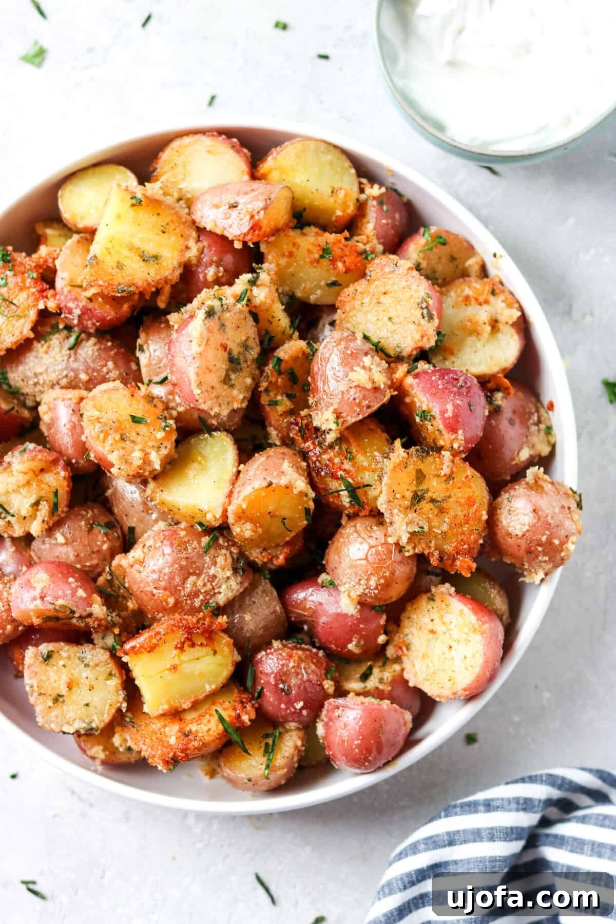 Parmesan Crusted Crispy Potatoes 2 A bowl of golden crispy Parmesan potatoes, perfectly roasted and ready to be served, with a side of creamy sour cream for dipping.