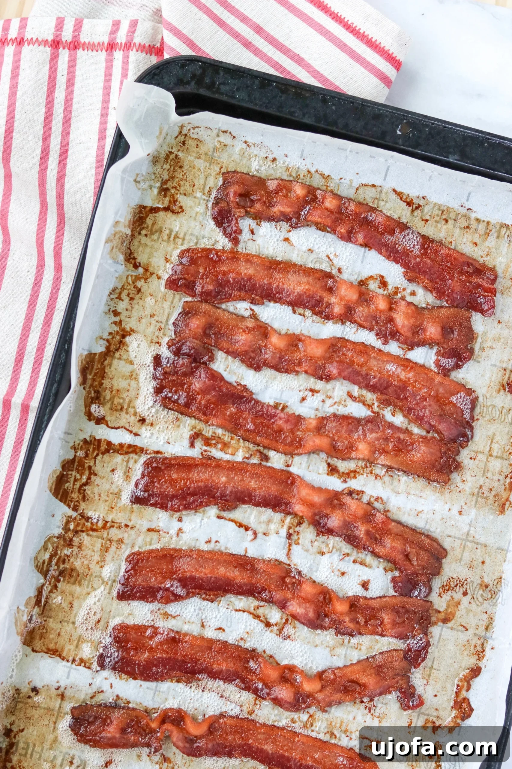 Crispy Baked Bacon, Zero Cleanup 3 Two hands placing raw bacon strips onto a parchment-lined baking sheet, preparing for oven baking.