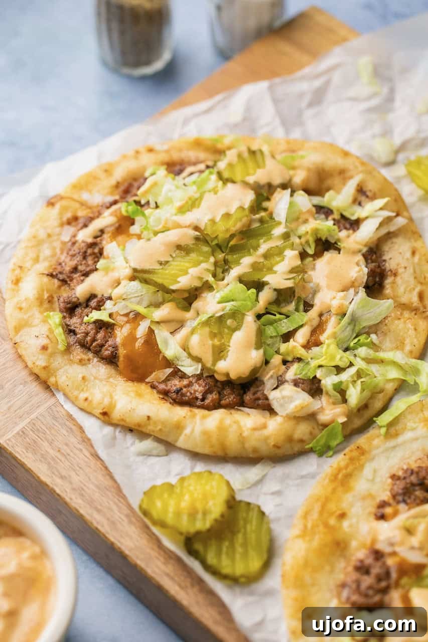 A close-up of beautifully plated Big Mac tacos, garnished with fresh lettuce, tangy pickles, melted cheese, and a swirl of signature Big Mac sauce, presented on parchment paper.