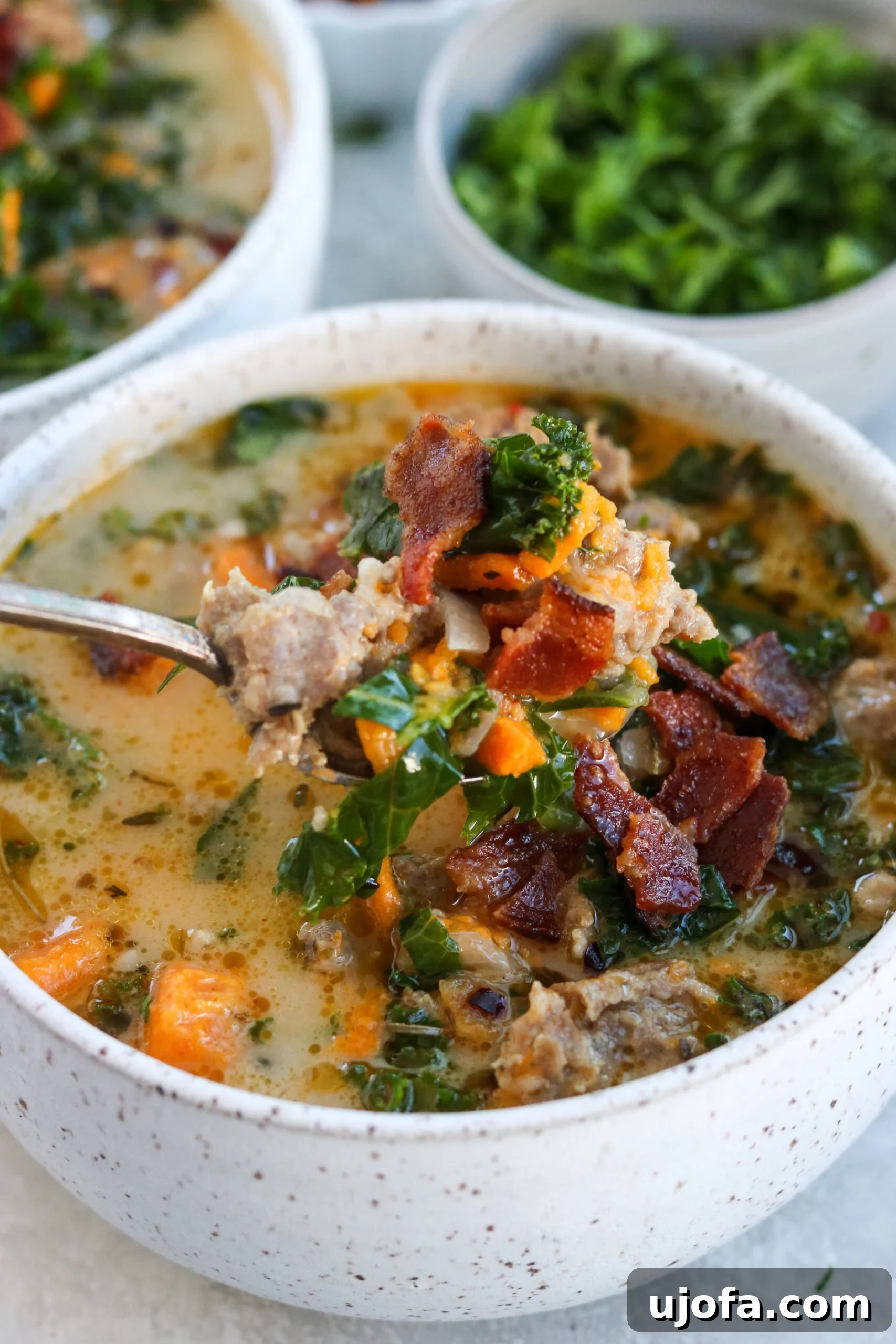 Whole30 Paleo Zuppa Toscana 7 A close-up of a spoonful of Healthy Whole30 Zuppa Toscana, showing delicious chunks of sausage, sweet potatoes, and kale, topped with crumbled bacon.